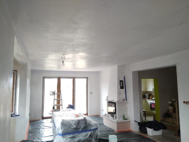 Salon w trakcie remontu – zabezpieczone meble folią, ściany i sufit po gładzi gipsowej, przygotowanie do malowania.